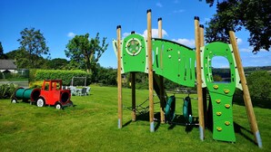 A playground with a green climbing structure, a red vehicle, and a grassy field.