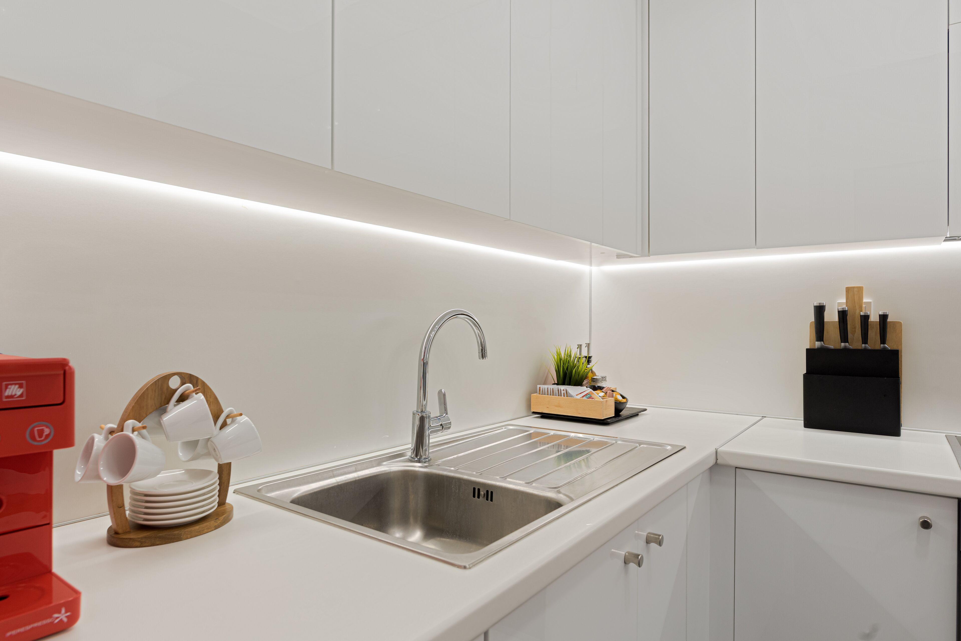 A modern kitchen with a stainless steel sink, white cabinets, and a red coffee machine.