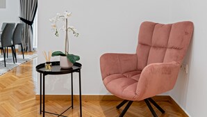 A modern room with a round mirror, a pink chair, a small table with a plant, and a wooden floor. - Kolonaki Luxury Residence (Athens)