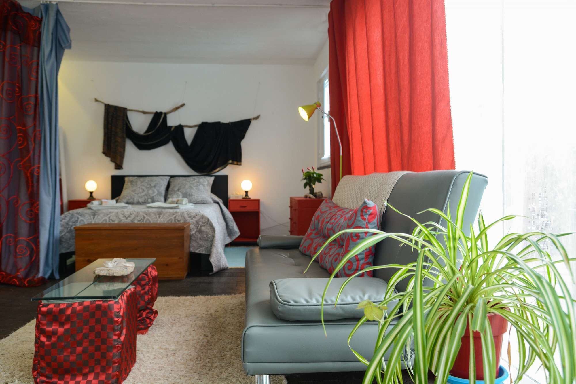 A bedroom with a bed, a sofa, a table, and a potted plant.