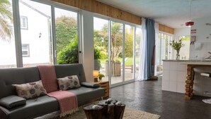 A modern living room with a grey sofa, a wooden coffee table, and a large sliding glass door leading to a garden.