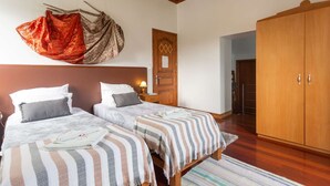 A bedroom with two beds, a wooden wardrobe, and a hanging garment. - Two-level marvel in exotic fruit orchard (Ribeira Grande)