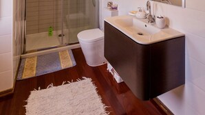 A modern bathroom with a glass-enclosed shower, a white sink with a dark countertop, and a large mirror above the sink. - Two-level marvel in exotic fruit orchard (Ribeira Grande)
