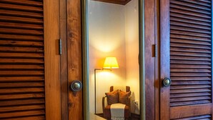 Una puerta de madera con un espejo que refleja una habitación con una lámpara, una cama y una mesita.