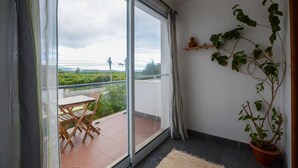 Un balcón con una mesa y sillas, una planta en maceta y vistas a zonas verdes y líneas eléctricas.