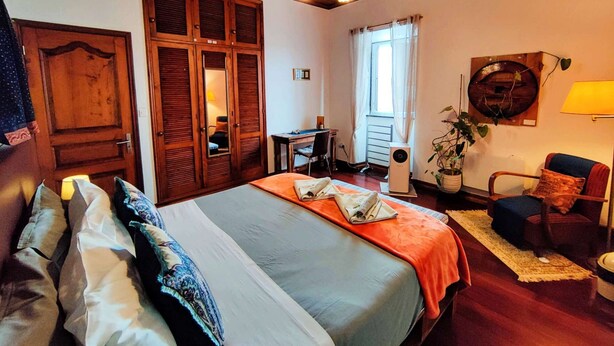 Una habitación con una cama, un escritorio, una silla, una planta en maceta y una lámpara de pared.