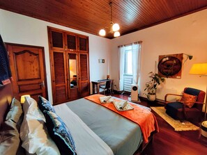 Una habitación con una cama, un escritorio, una silla, una planta en maceta y una lámpara de pared.