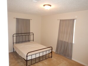 Een slaapkamer met een enkel metalen bed, beige wanden en een plafondlamp.