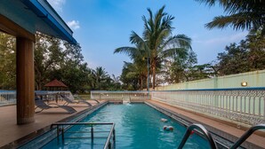 A swimming pool with a metal ladder, lounge chairs, and a small gazebo. - Geeta Bhawan (Karjat)