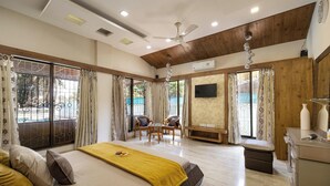 A spacious bedroom with a large bed, a seating area with chairs, a TV, and a balcony with curtains. - Geeta Bhawan (Karjat)
