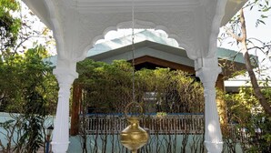 A white, ornate pavilion with a central fountain, surrounded by lush greenery and a decorative fence. - Geeta Bhawan (Karjat)