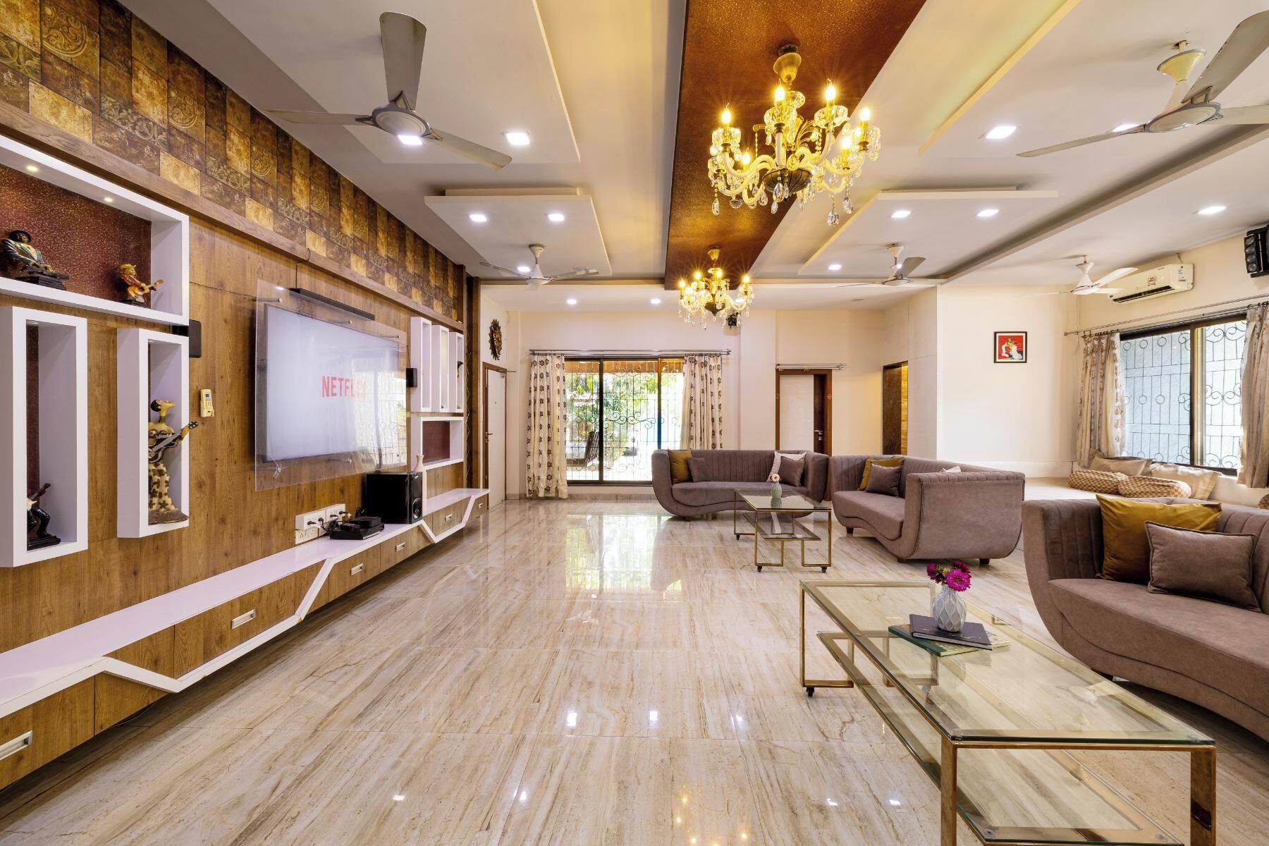 A spacious living room with a large flat-screen TV, comfortable seating, a chandelier, and a ceiling fan.