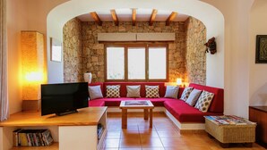 A cozy living room with a stone wall, a red sofa, a wooden coffee table, and a TV on a wooden stand. - rose village (Sant Josep de sa Talaia)