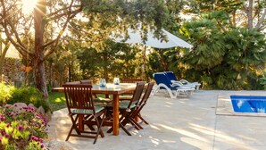 A patio area with a dining table and chairs, a pool, and a white umbrella. - rose village (Sant Josep de sa Talaia)