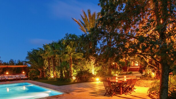 A pool area with a table and chairs, surrounded by trees and illuminated by warm lighting. - rose village (Sant Josep de sa Talaia)