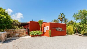 A red building with a spiral design, surrounded by gravel, plants, and trees. - rose village (Sant Josep de sa Talaia)