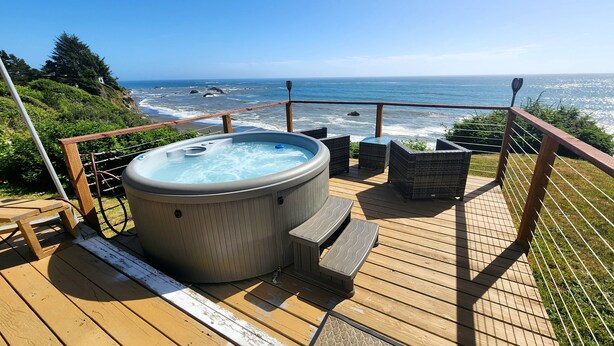 A wooden deck with a hot tub, wicker chairs, and a view of the ocean.