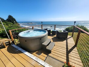 A wooden deck with a hot tub, wicker chairs, and a view of the ocean. - Charming Oceanfront Cottage; Stunning Ocean Views, Hot Tub & Nearby Beach Access (Brookings)