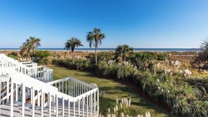 Ein strandnahes Anwesen mit einer weißen Holzdielenveranda, Palmen und Meerblick.