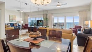 Ein geräumiges Wohnzimmer mit Glaswand, ein Essbereich mit Glastisch und ein Balkon mit Meerblick.