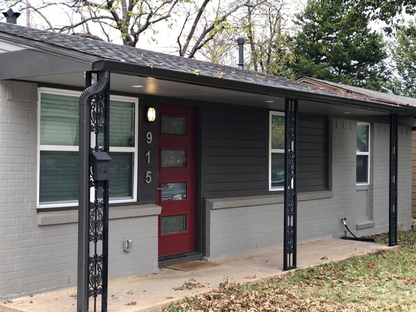 Une maison de plain-pied avec une porte d’entrée rouge, portant le numéro 915, et un petit porche.