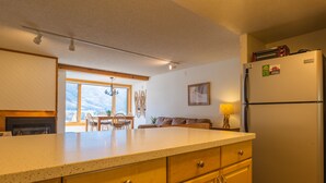 Una cocina con armarios de madera, un refrigerador y una zona de comedor con una mesa y sillas.