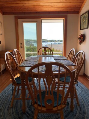 Un comedor con una mesa redonda y seis sillas, vista a través de un ventanal y techo de madera.