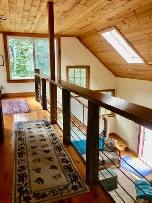A wooden interior with a high ceiling, a long wooden staircase, and a view of greenery outside. - Dyers Hideout Cottage Beautiful Dyers Island (Vinalhaven)
