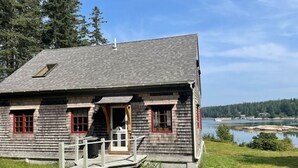 A wooden cabin with a small porch and a dock, overlooking a lake and forest. - Dyers Hideout Cottage Beautiful Dyers Island (Vinalhaven)
