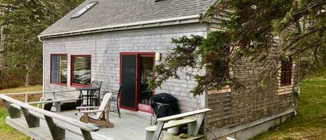 A small cabin with a deck, outdoor seating, and a barbecue grill.