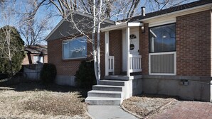 A two-story brick house with a front porch, a visible door, and a small front yard. - Anna's Alley Cute top floor 3 BD/ House Heart of SLC (Murray)