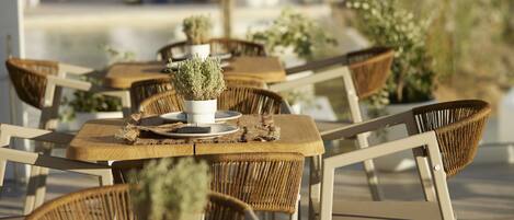 Un espacio de comedor al aire libre con sillas y mesas de mimbre, cada uno decorado con una planta en maceta.