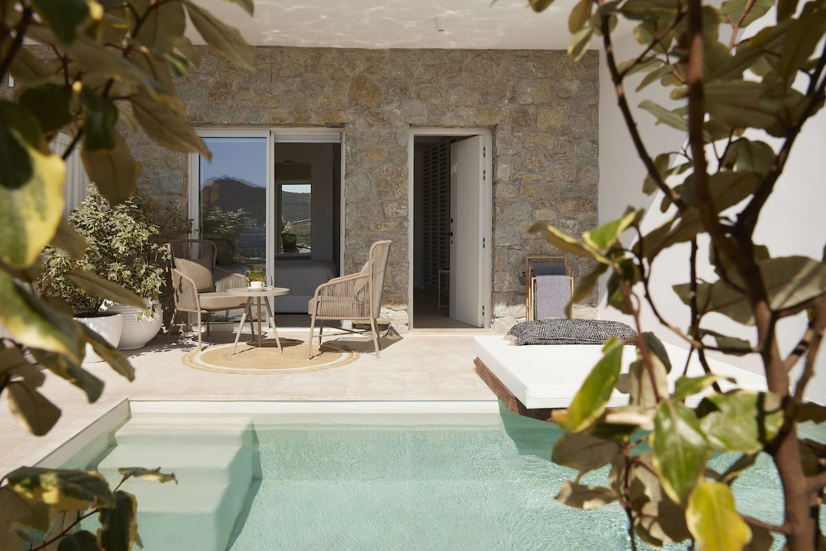 Un espace aménagé au bord de la piscine, avec un mur en pierre, deux fauteuils en osier, une petite table et une vue sur l’extérieur.