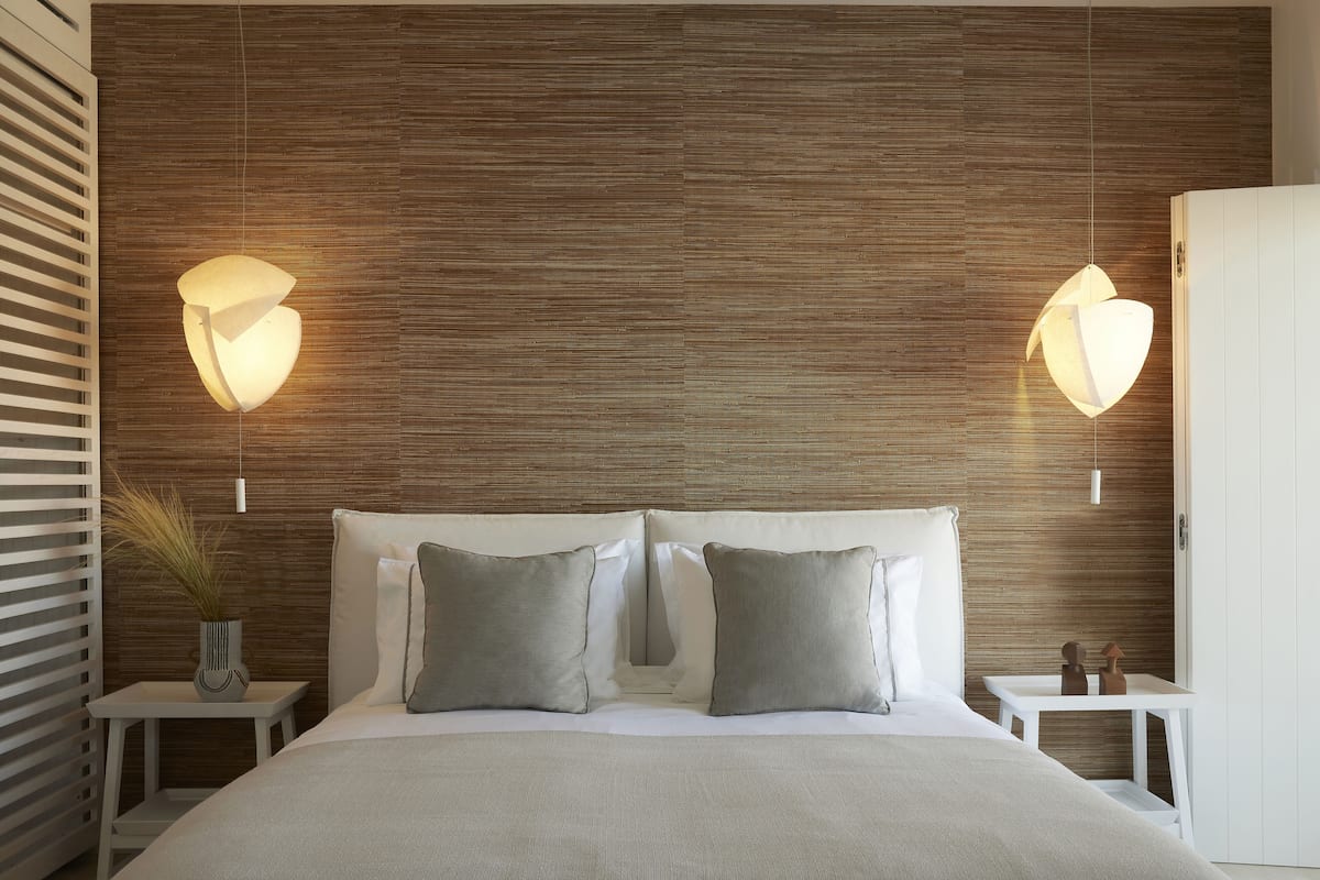 Une chambre à coucher moderne avec une tête de lit en bois, deux tables de chevet et un grand lit recouvert d’une couvre-lit aux couleurs neutres.