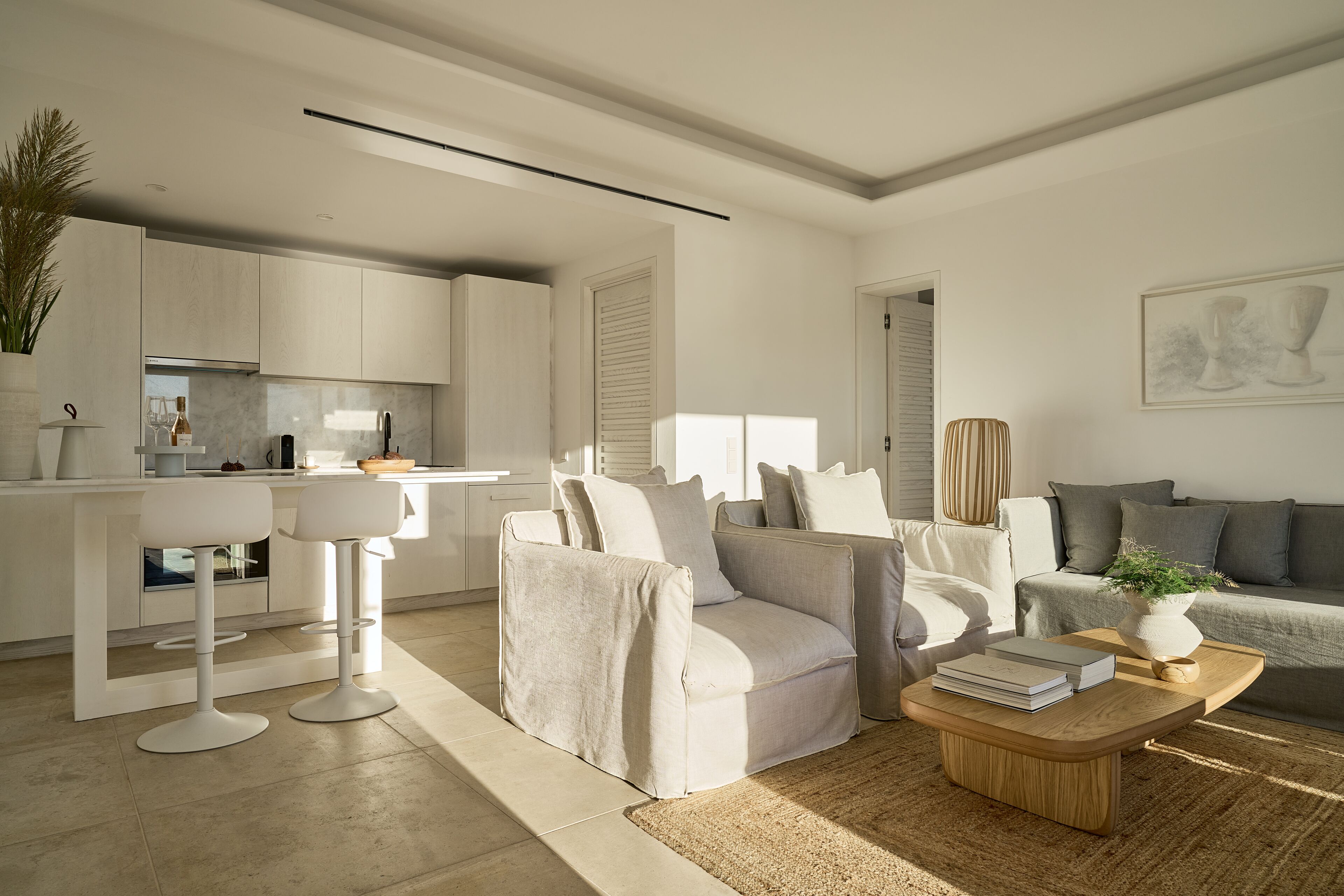 Een moderne woonkamer met een bank, salontafel en barstoelen. Er is een keukenhoek met kastjes en een aanrecht.