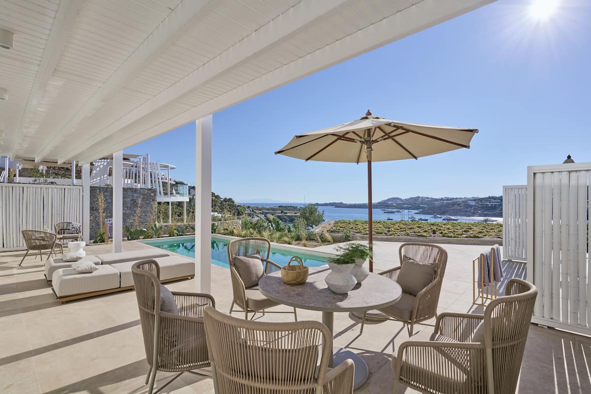 Un espace extérieur abrité, aménagé avec des meubles en osier, une piscine et offrant une vue panoramique sur la côte.