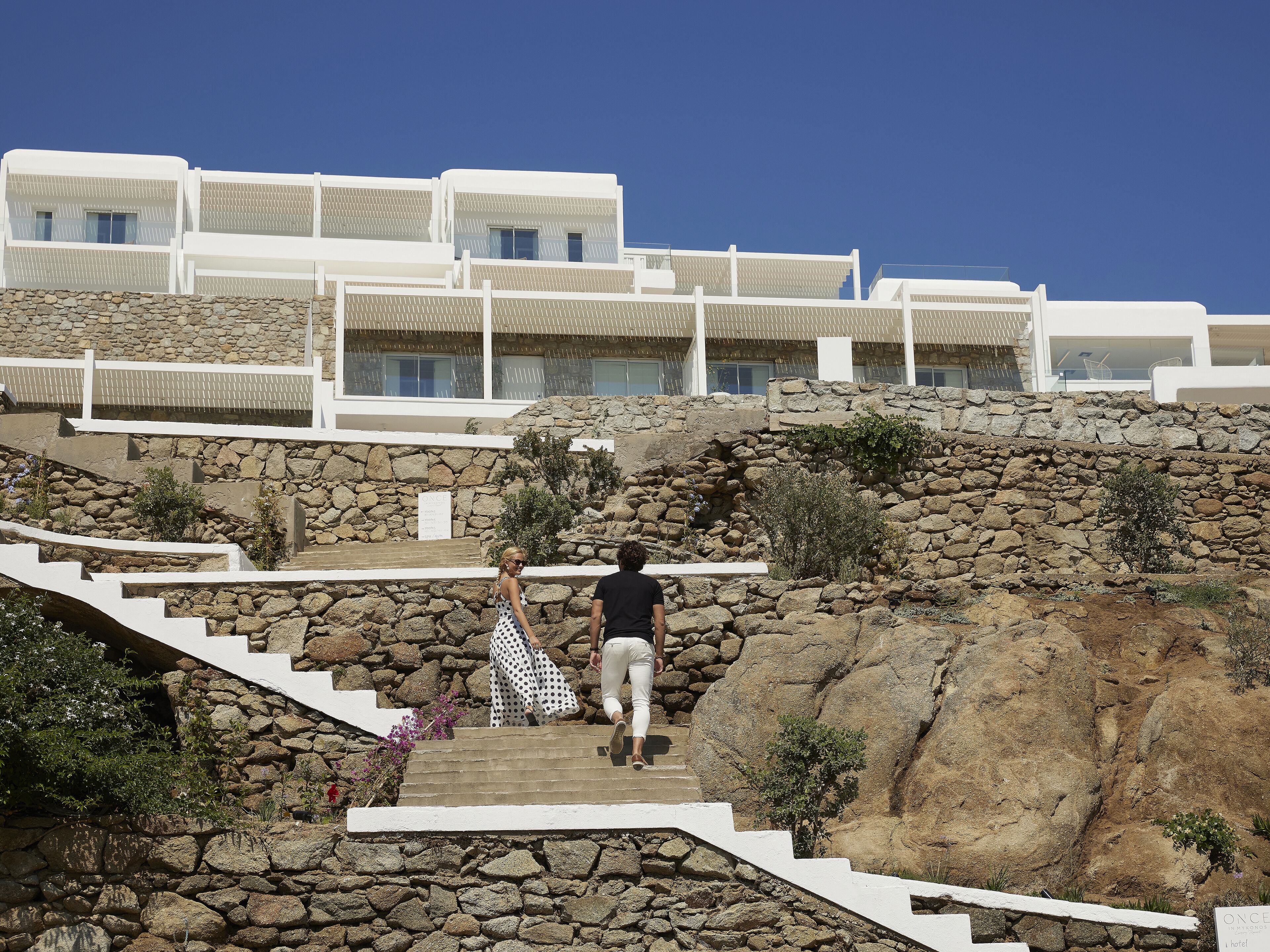 A hotel with stone walls and white balconies, featuring a staircase leading to the upper floors.