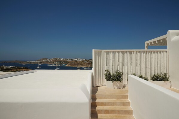 A white building with a staircase leading to a terrace overlooking the sea.