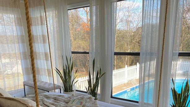 Un dormitorio con cama de madera, ropa de cama blanca y vista a una piscina.