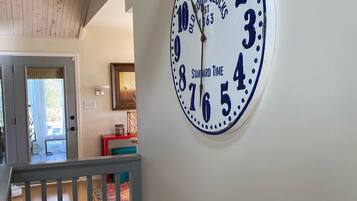 A wall-mounted clock with a classic design, a staircase with a wooden railing, and a glimpse of a room with a window and a door.