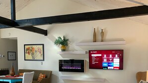 Una sala de estar moderna con un televisor de pantalla plana grande montado en la pared, un sofá cómodo, una mesa de centro y una cama cubierta con un sábana blanca.