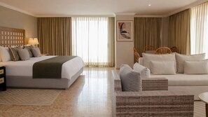 Une chambre d’hôtel avec un lit, un canapé, une chaise, une table de chevet et une lampe.