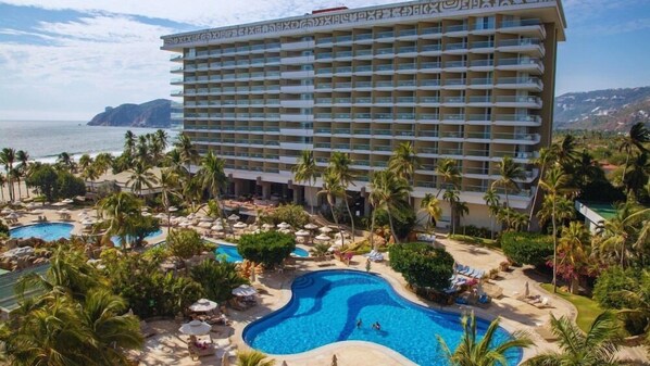 Un hôtel doté de nombreux balcons, d’un espace piscine avec des chaises longues et offrant une vue sur l’océan.
