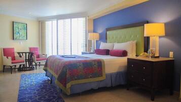 A hotel room with a large bed, two bedside lamps, a small desk with a chair, and a window with blinds.