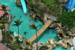 A rope bridge over a turquoise pool with palm trees and rocky formations. - Princess Mundo Imperial (Acapulco)
