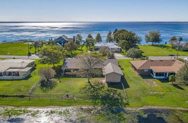 An aerial view of a residential area with houses, a grassy field, and a body of water in the background.