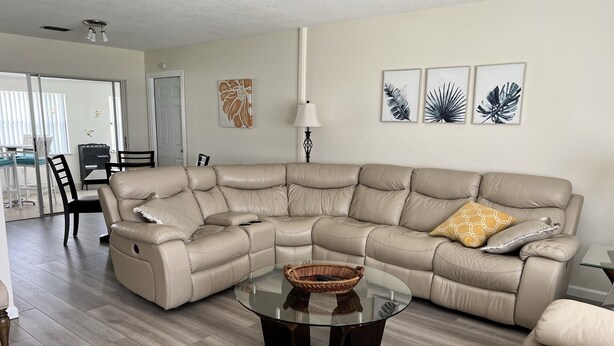 A spacious living room with a large beige sectional sofa, a glass coffee table, and a dining area with a table and chairs. - A perfect place in Central Florida for boating, fishing, or a relaxing vacation! (Lake Wales)