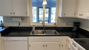 A kitchen with white cabinets, a stainless steel sink, a dishwasher, a stove, and a window with a view of trees and a fence. - A perfect place in Central Florida for boating, fishing, or a relaxing vacation! (Lake Wales)