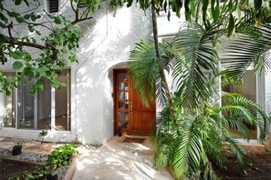 Ein Haus mit weißer Fassade, einer Holztür und einem kleinen Garten mit Pflanzen.