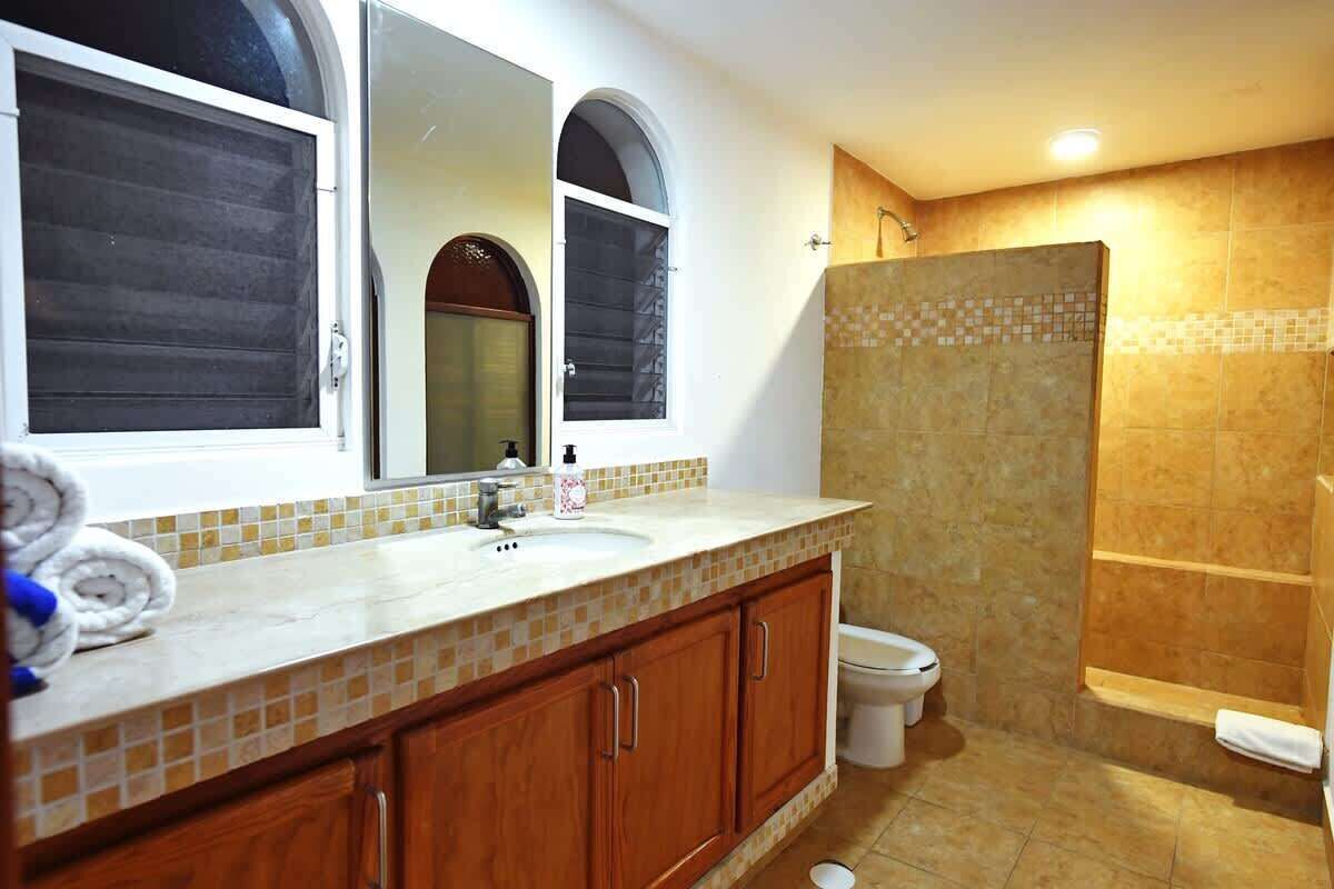A bathroom with a double sink, a mirror, a shower, and a toilet.